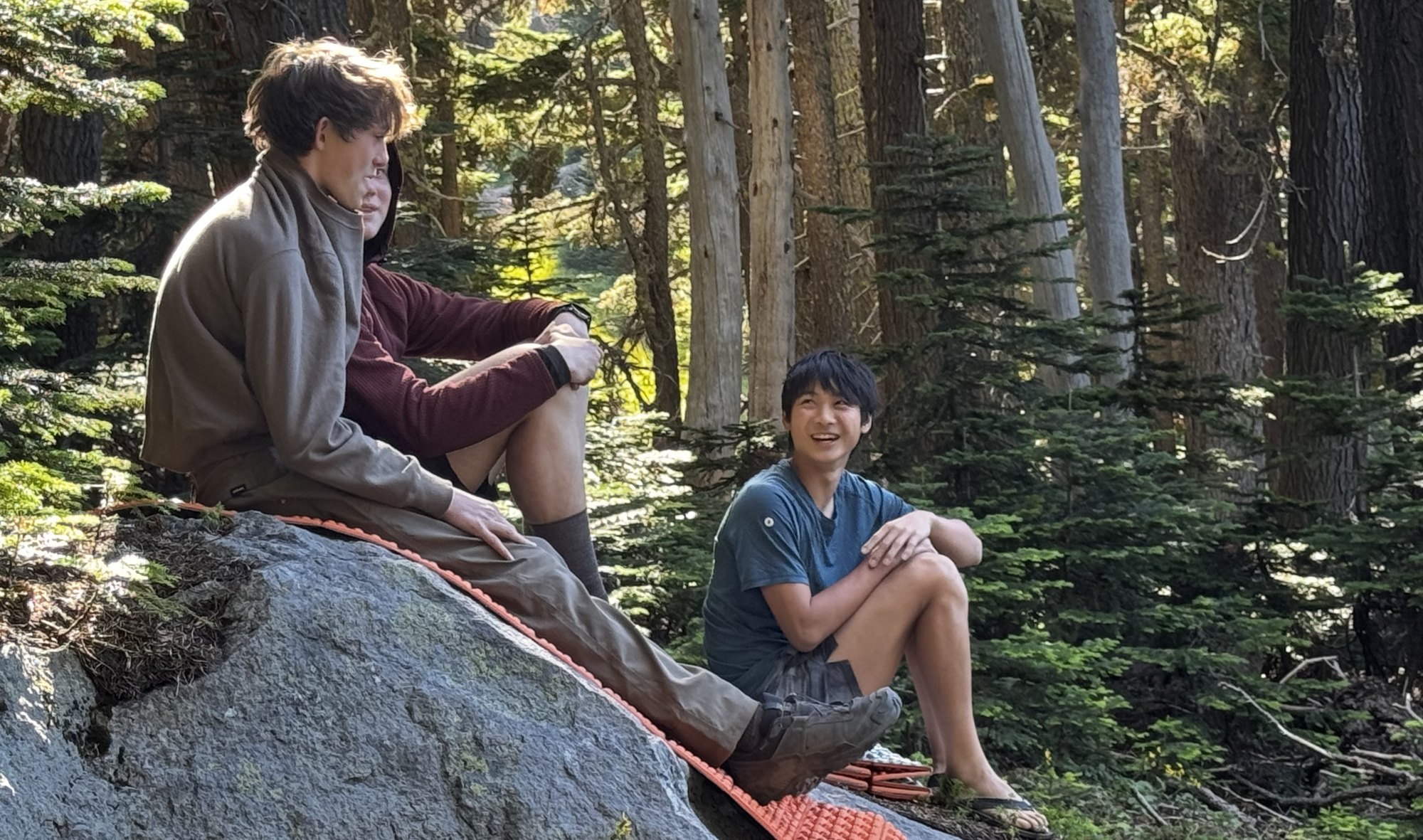 Two boys resting and talking on a rock in the forest